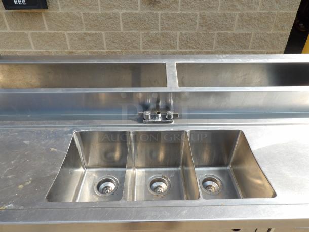Stainless steel triple-basin sink with dual faucets, professional kitchen grade, in good condition, slight surface wear.