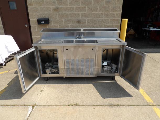 Stainless steel commercial sink station, two basins, open storage doors, mounted on wheels; suitable for kitchen use.