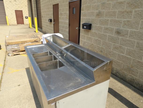 Stainless steel commercial bar sink with four compartments, good condition. Features raised backsplash and two faucets.