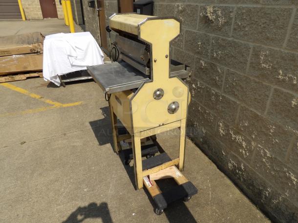 Vintage industrial paper cutter in yellow, with metal blade and plate. Moderate wear, sturdy design, mounted on wheels.