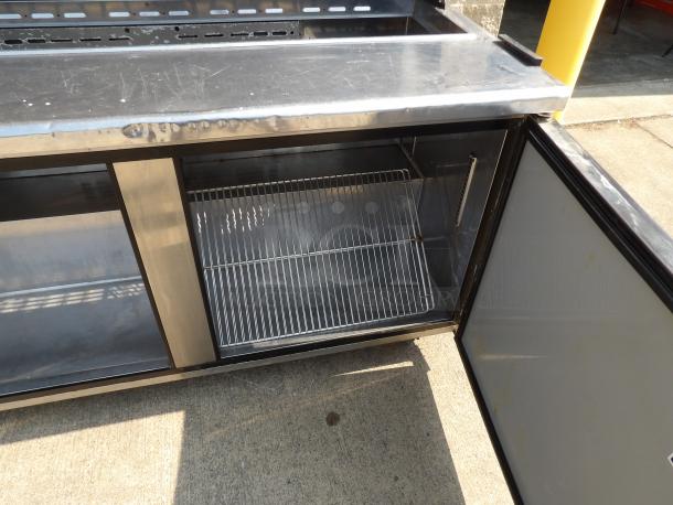 Stainless steel commercial refrigerator with open door, interior wire shelf, minor surface scratches. Suitable for catering use.
