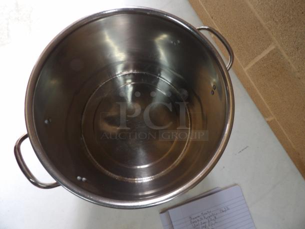 Large stainless steel stockpot with dual handles, in good condition, placed on a table next to a notebook with handwritten notes.