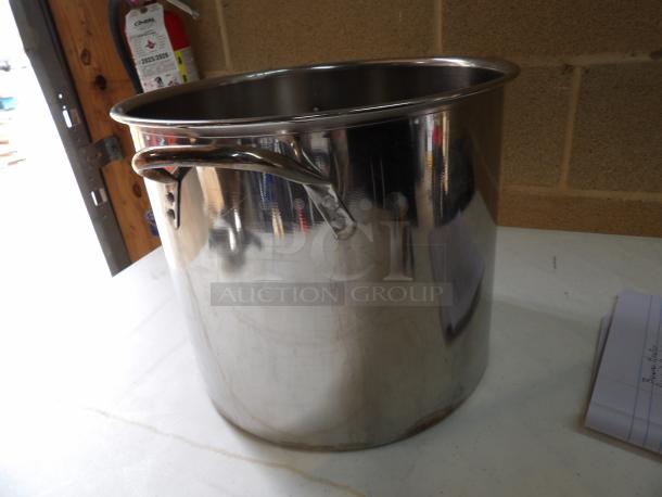 Stainless steel stock pot with handles, large capacity, reflective surface, in good condition, on a white table.