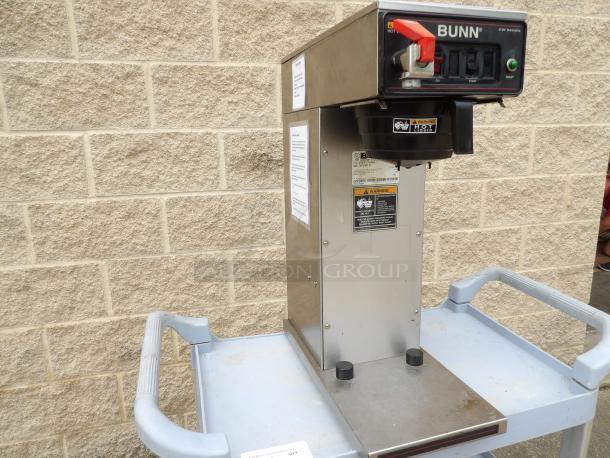 Bunn CW Series coffee brewer on metal cart, stainless steel, visible warning labels, features on/off and start switch.