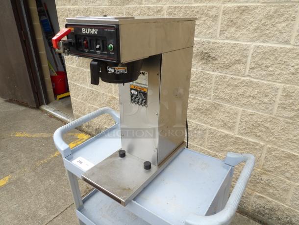 Bunn CW Series coffee brewer, stainless steel, used condition, visible warning labels and control panel, on gray cart.