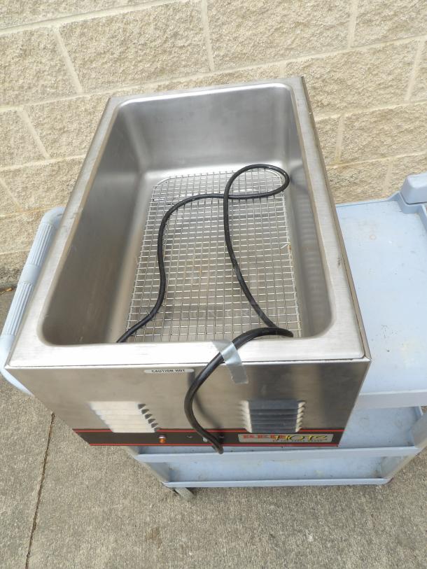 Stainless steel food warmer with heating element, caution label, and power cord. Used condition. Measures approx. 24x12 inches.