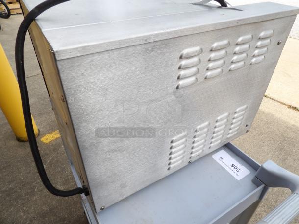 Industrial metal equipment with vents on the side, visibly used, black cable attached. Tag shows "306".