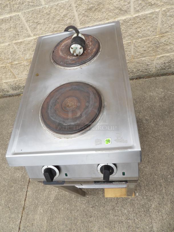 Stainless steel dual burner electric stove with visible wear. Two control knobs, top marks, and a plug are evident.