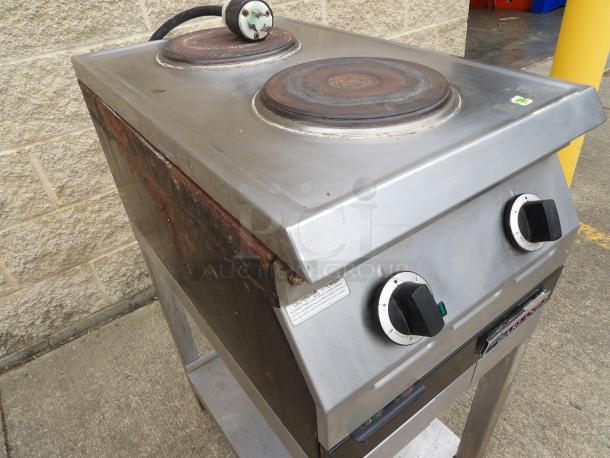 Commercial two-burner hot plate in fair condition, featuring manual dials and a metal stand with visible rust and wear.