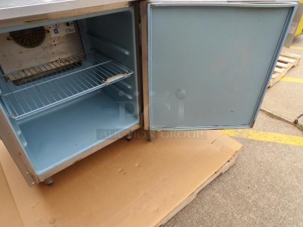 Stainless steel commercial refrigerator, single door, blue interior, wire shelf, visible wear, no brand label.