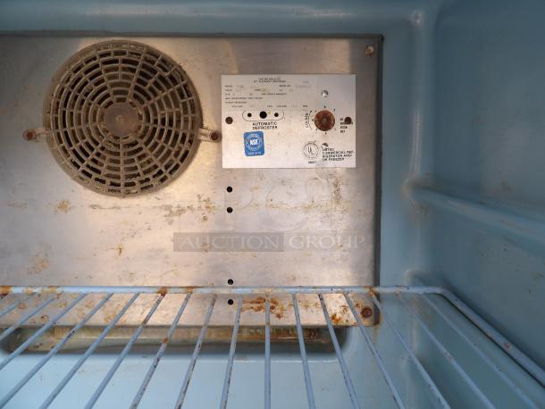 Vintage commercial refrigerator interior with metal shelf, cooling fan, and defrost control panel. Visible wear and rust.