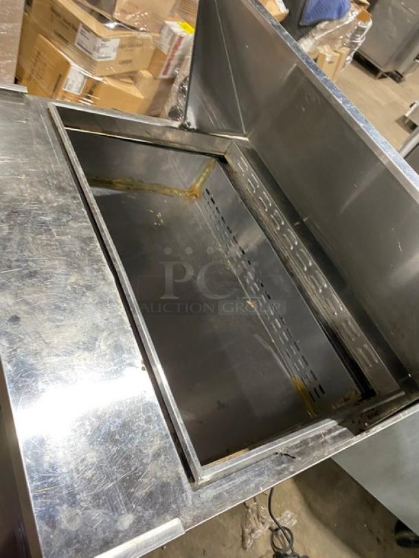 Stainless steel commercial refrigerator unit with open interior, top lid, visible wear, ideal for restaurant use.