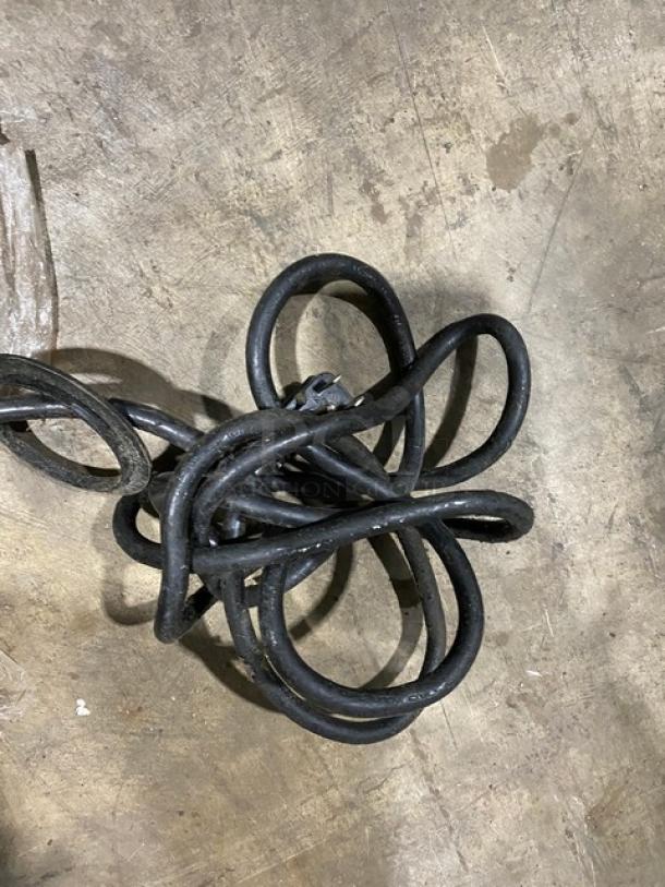 Coiled black rubber hose on a concrete floor, in used condition, with visible wear and no labels or tags attached.