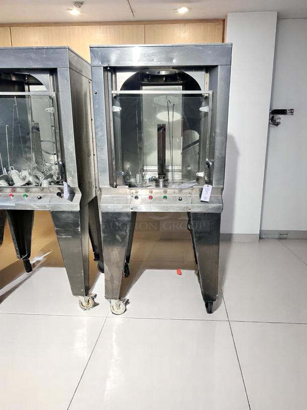 Commercial stainless steel rotisserie machine with glass door, used condition, on caster wheels. Control panel with labels.