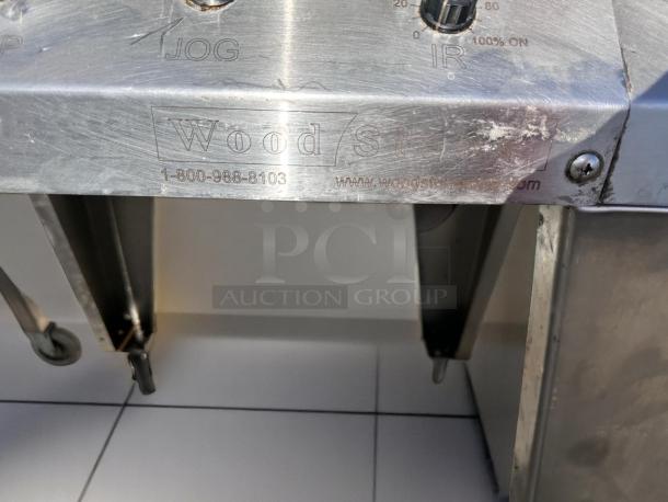 Stainless steel commercial appliance with "Wood" branding and control dials, showing signs of wear, engraved contact details.