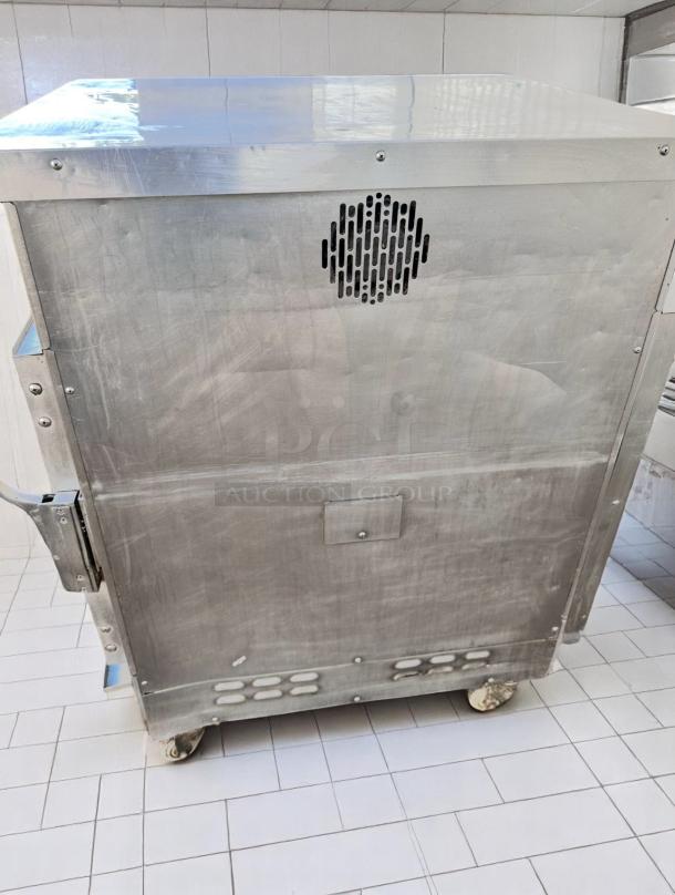 Industrial stainless steel oven on casters, showing ventilation grates and handles. Slightly scuffed surface.