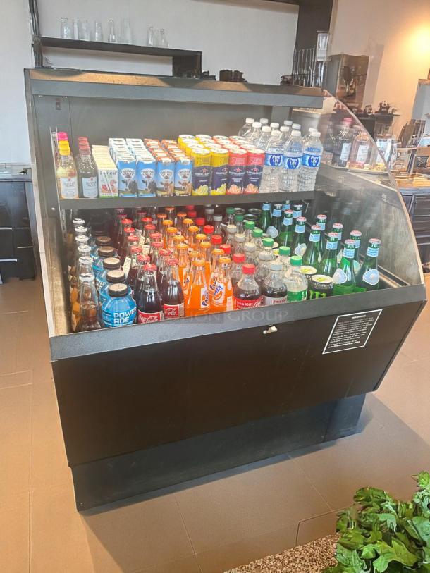 Black beverage cooler stocked with assorted drinks, including water, sodas, and juices. Two glass shelves, clean condition.