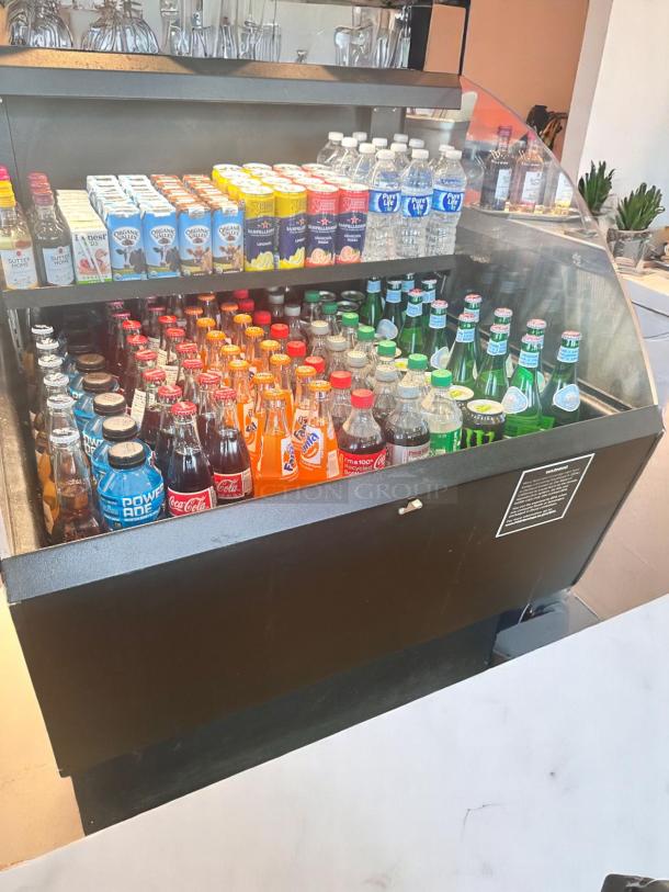 Refrigerated display case with assorted beverages, including bottled water, soda, and juice boxes, in new condition.