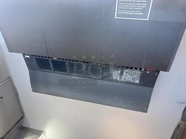 Commercial black wall-mounted range hood with a warning label. Features vent slats and visible wear.