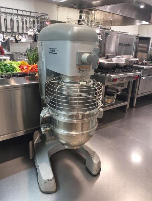 Hobart industrial mixer in a commercial kitchen, large capacity, sturdy metal build, safety guard, good condition.