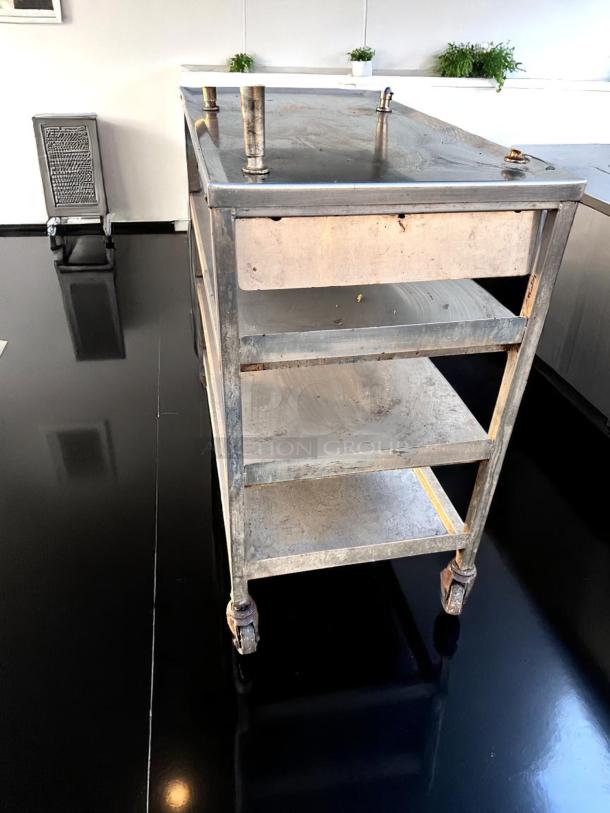 Industrial stainless steel utility cart with three shelves and wheels, showing signs of wear and rust, ideal for commercial use.