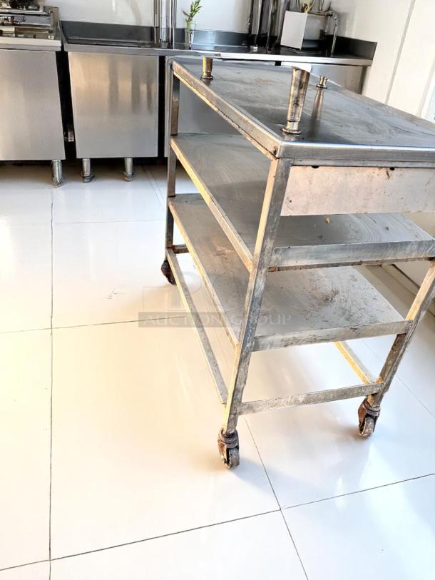 Stainless steel kitchen cart with three shelves and wheels, showing signs of wear and rust.