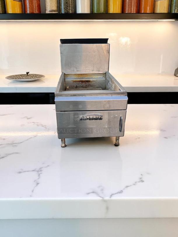Stainless steel countertop fryer with open lid, used condition, adjustable legs, and front panel logo. Suitable for small kitchens.
