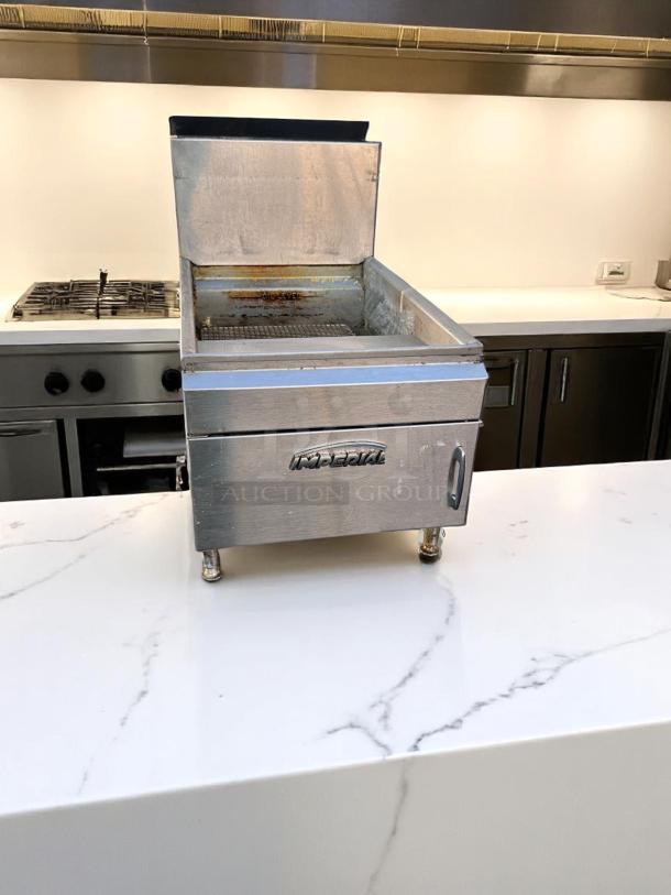 Stainless steel Imperial deep fryer, used condition, featuring open lid and visible oil residue, on marble counter.
