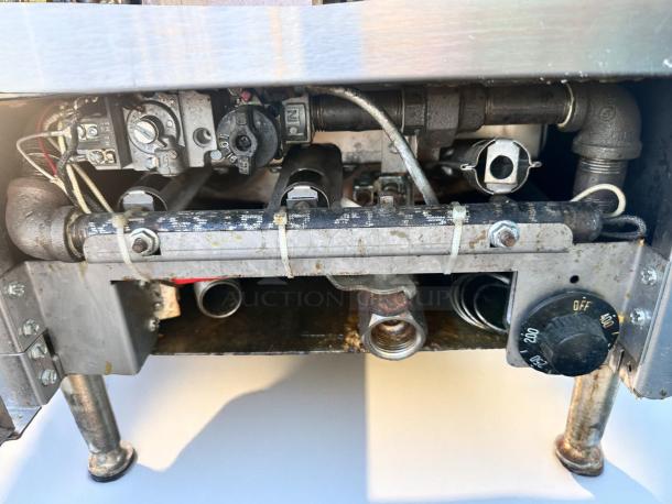Industrial gas burner control system with visible valves, pipes, and adjustment knob. Shows signs of use and minor rust.