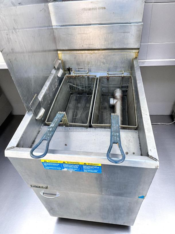 Stainless steel commercial deep fryer with two baskets, "Pitco" brand, visible wear, caution labels in multiple languages.