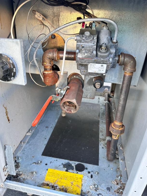 Commercial gas furnace interior showing exposed piping, valves, and a thermostat. Visible rust, wear on components.