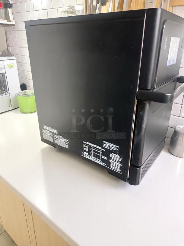 Black microwave on countertop, featuring control panel on the side. Labels with operating instructions and safety warnings visible.