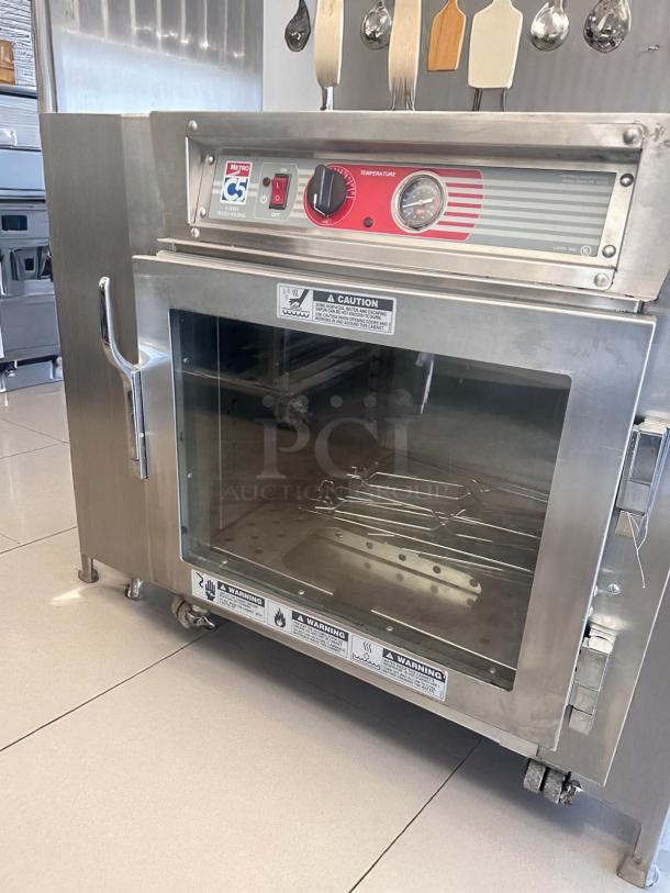 Industrial Metro C5 heated holding cabinet, stainless steel, temperature gauge, glass door, safety warnings visible.