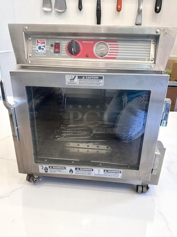 Metro C5 3 Series heated holding cabinet with glass door and temperature gauge, in good condition. Warning labels visible.