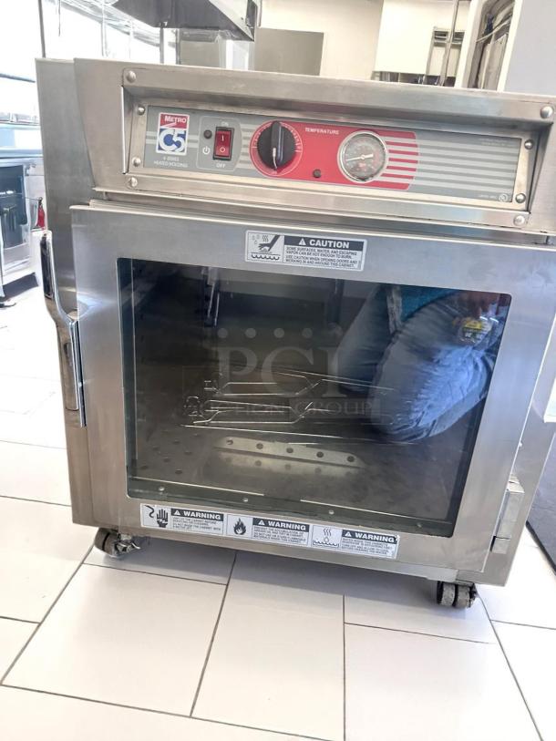 Metro C5 heated holding cabinet, stainless steel, front glass door, temperature control dial, caution labels, on casters.
