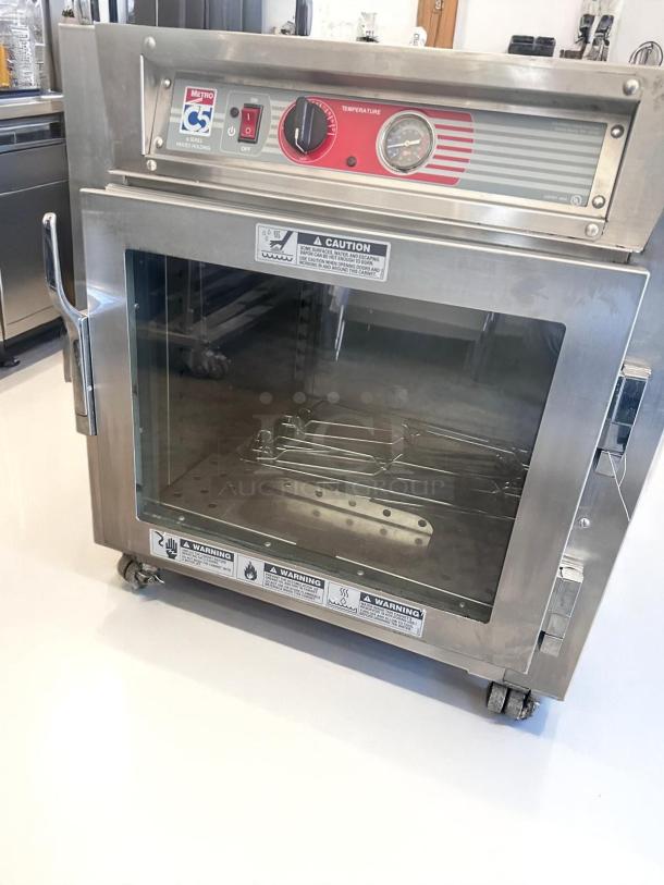 Metro C5 heated holding cabinet, stainless steel, clear glass door, temperature dial, caution and warning labels visible.