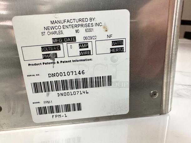 Metal device by Newco Enterprises with a label showing serial DN00107146, model FPM-1, dated 06/29/22.