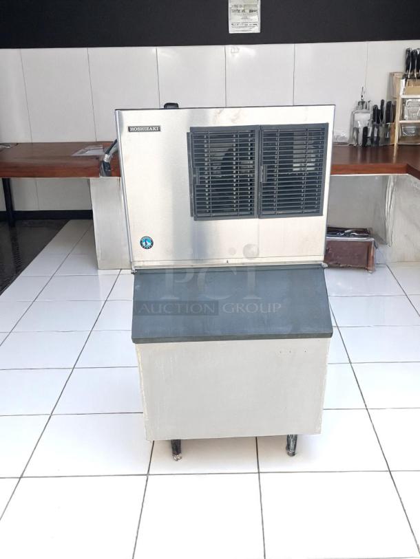 Hoshizaki ice maker with stainless steel finish, fan vents, placed on a tiled surface. Slight signs of wear visible.