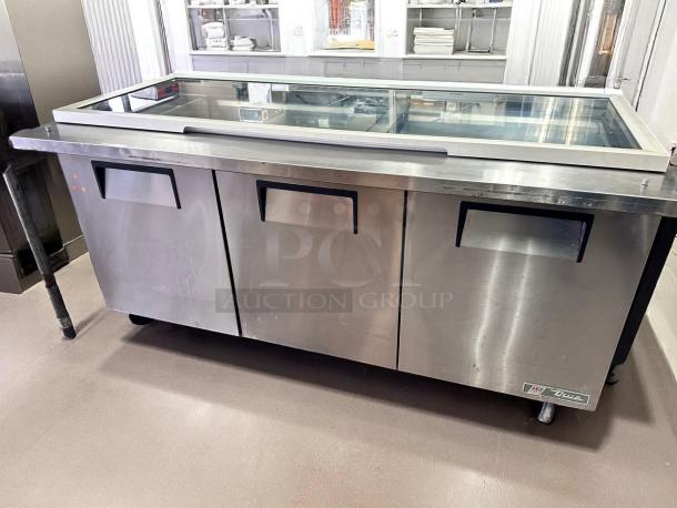 Commercial stainless steel refrigerated prep table with three doors and glass top, True brand, good condition.
