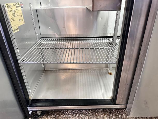 Commercial stainless steel refrigerator with two wire shelves, True brand, model 8317129, shows light wear and rust spot.