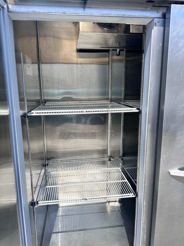 Commercial stainless steel refrigerator with two wire shelves, clean interior, and visible inspection label on the left.