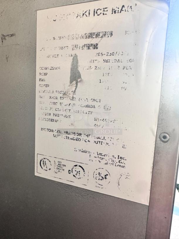 Worn manufacturer label on an industrial ice machine, showing specifications and warnings. Edges slightly torn and faded.