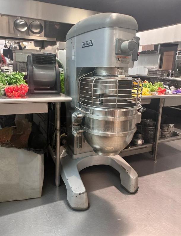 Hobart industrial mixer in a commercial kitchen. Features stainless steel bowl, safety guard. Used condition.