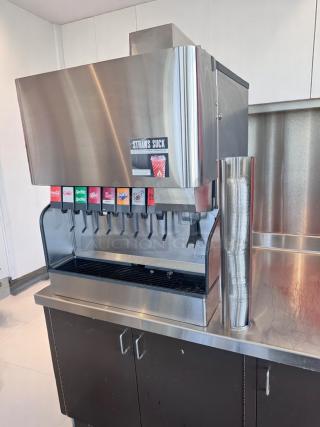 Commercial beverage dispenser with eight labeled soda options, stainless steel finish, straw holder, and "Straws Suck" sticker.