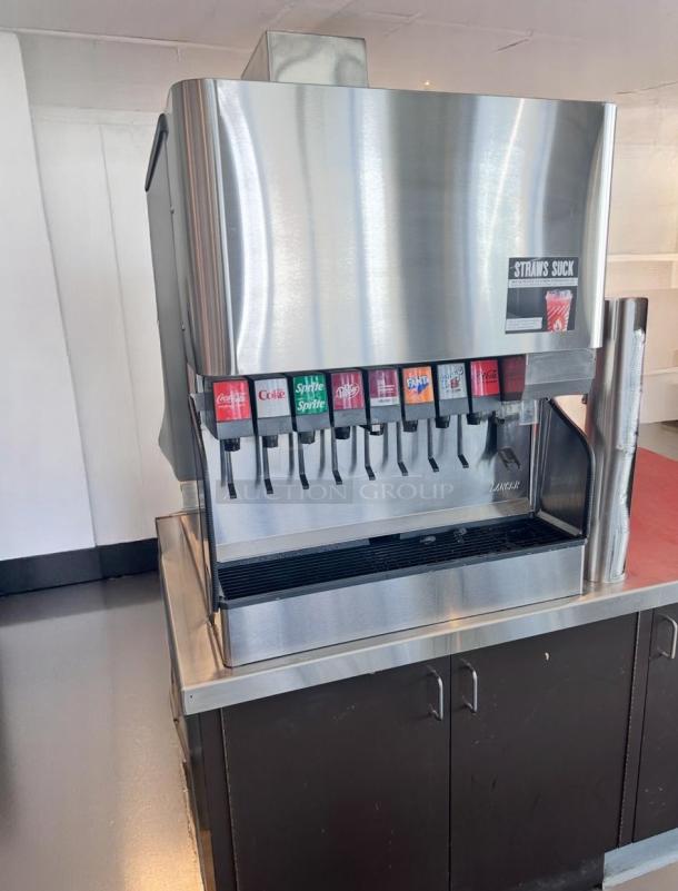 Lancer soda fountain dispenser, stainless steel, 8 drink options, "STRAWS SUCK" label. Mounted on dark cabinet, appears in good condition.