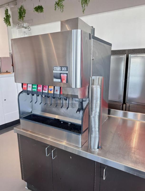 Commercial soda dispenser with eight drink options, stainless steel finish, cup holder on the side, and a "Straws Suck" sticker.