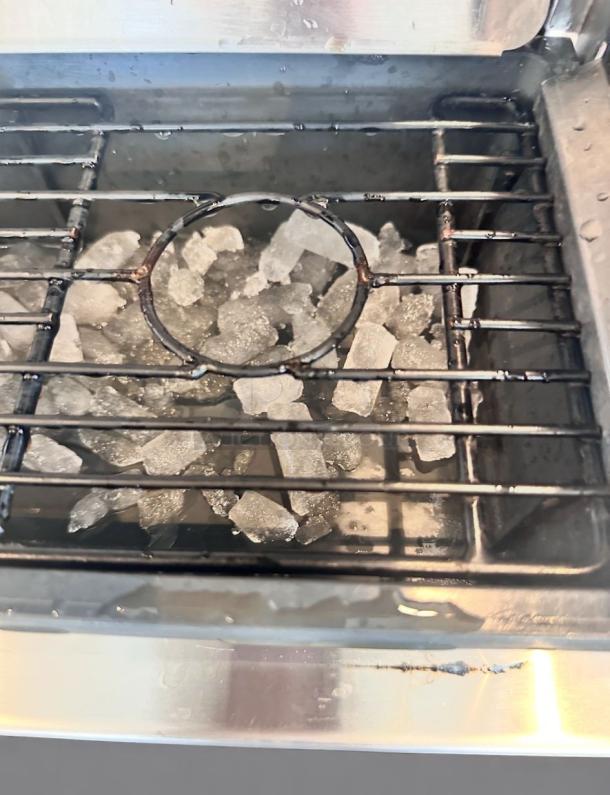 Stainless steel grill with built-in ice compartment, used condition, featuring a metal grate and visible water droplets.