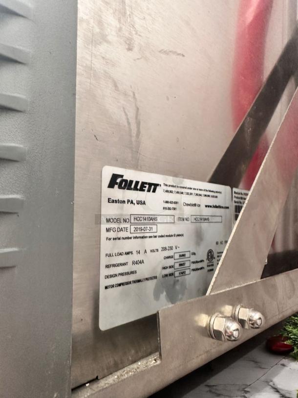 Follett refrigerator unit, model HCC1410AHS, manufactured 2019-07-31, uses R404A refrigerant. Visible wear on metal.