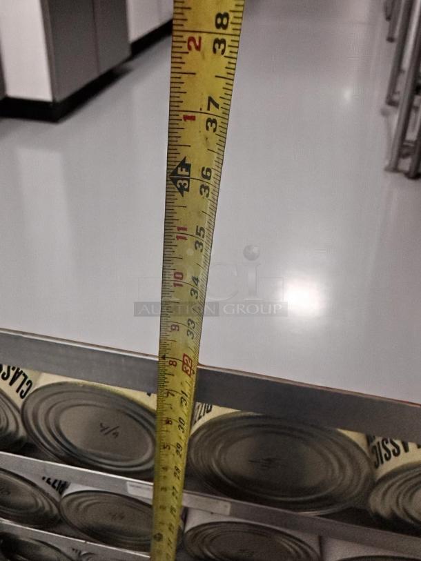 Tape measure extended over stacked cans, reading 35 inches. Cans below marked "1/4". Clean, reflective floor.
