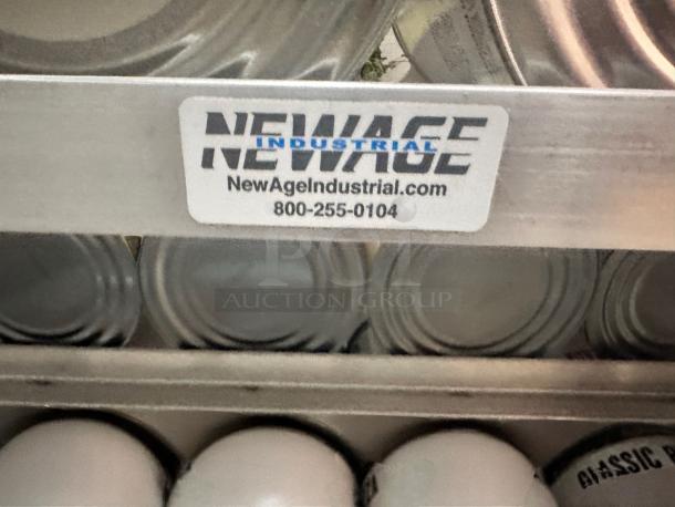 NewAge Industrial shelving label with website and contact number; visible rows of stored cans below.